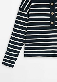 Chemise à manches longues rayée horizontale bleu marine et blanc avec une patte de boutonnage partielle comportant quatre boutons métalliques.