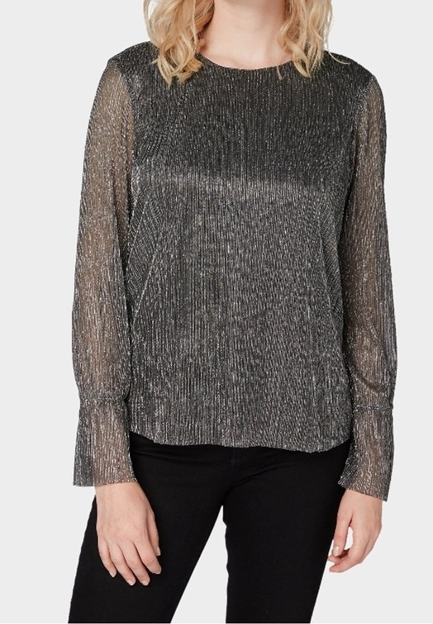 Frau trägt eine langärmlige, durchsichtige, metallisch schwarze Bluse mit rundem Ausschnitt und strukturierten, vertikalen Streifen.