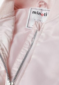 Veste zippée rose clair en matériau brillant, avec un col côtelé et un détail de fermeture éclair argenté, étiquetée en taille 3-4 ans.