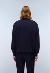 Marineblauwe sweatshirt met een ontspannen pasvorm, rib gebreide manchetten en tailleband, gemaakt van zachte stof. Achteraanzicht toont een glad, minimalistisch ontwerp.