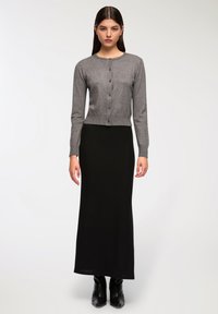 Cardigan grigio lavorato a maglia con scollatura rotonda e chiusura a bottoni, abbinato a una lunga gonna nera a costine. Stivali neri alla caviglia completano il look.