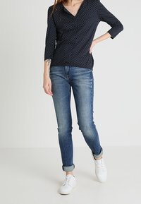 Námořnická halenka s puntíky a třičtvrtinovými rukávy, spojená s džíny v středním odstínu a bílými teniskami. Neformální outfit vhodný pro různé příležitosti.