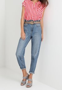 Punavalkoraidallinen lyhythihainen pusero, vaaleansiniset käännetyt farkut, harmaa vyö, jossa on kaksinkertainen pyöreä solki, sekä mustavalkoraidalliset korkokengät.