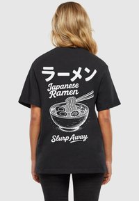 Must have mustekas T-särk, millel on valge graafiline joonistus ramen-kausid, tekstiga jaapani ja inglise keeles, ning lõtva lõikega. Lühikesed varrukad ja pehme tekstuur.