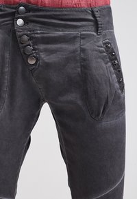 Zwarte katoenen broek met een hoge tailleband, een sluiting met vijf knopen, en decoratieve stervormige accenten op de zijzakken.