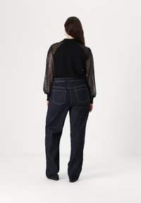 Μαύρη μπλούζα με παγιέτες στα μανίκια, συνδυασμένη με σκούρες μπλε ψηλόμεσες τζιν που διαθέτουν πίσω τσέπες και ίσια γραμμή.