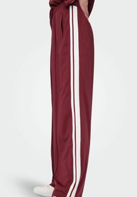 Bordeaux trackbukser med hvide side-striber, lavet af glat materiale, med elastisk talje og sidelommer for bekvemmelighed.
