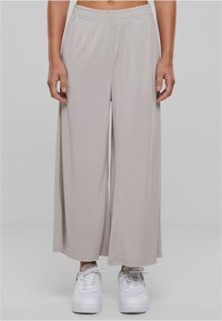 Pantaloni ampi grigi chiari realizzati in tessuto morbido e elastico con vita elasticizzata. Abbinati a sneaker bianche.