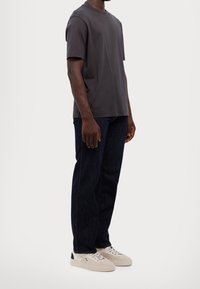 Dark grey cotton T-shirt with short sleeves, paired with dark blue straight-leg jeans and light sneakers featuring black accents.