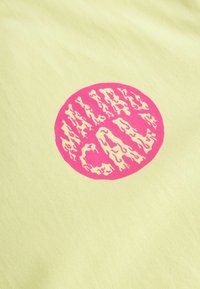 Tissu jaune avec un logo circulaire rose présentant le mot "HALF" au-dessus de "CAL" dans une police ondulée et stylisée.