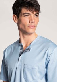 Lichtblauwe korte mouw shirt met een knoopsluiting, voorzien van een gemusterde paspelsectie en een zak op de linkerborst. Zachte stoftextuur.