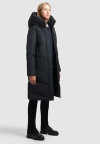 Schwarze Pufferjacke mit hohem Kragen und großer Kapuze, mit diagonalen Steppnähten, Druckknöpfen und seitlichen Taschen.