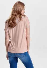 Lässig geschnittenes, kurzärmeliges T-Shirt aus weichem Blush-Stoff mit Rundhalsausschnitt und umgeschlagenen Ärmeln, kombiniert mit blauen Jeans.