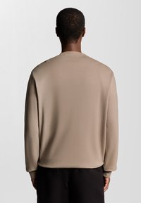 Beige langærmet top med rund halsudskæring og afslappet pasform. Glat tekstur, med sænkede skuldre og manchetter på ærmerne.