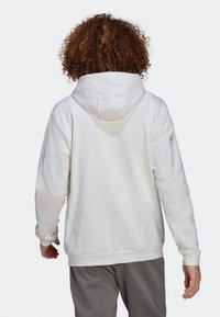 Sweat à capuche blanc avec une coupe décontractée, doté de poignets et d'un ourlet côtelés, d'une texture de tissu lisse, et d'une poche kangourou.