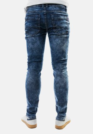 Blaue Denim-Jeans im Slim-Fit-Design, mit Gesäßtaschen und einem verwaschenen Finish. Kombiniert mit hellen Sneakers.