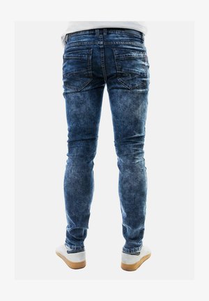 Blaue Denim-Jeans im Slim-Fit-Design, mit Gesäßtaschen und einem verwaschenen Finish. Kombiniert mit hellen Sneakers.