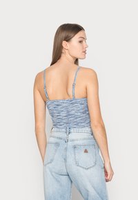 Top de tanque azul, canelado, com alças finas, apresentando um padrão texturizado. Combinado com jeans de ganga claros de cintura alta.