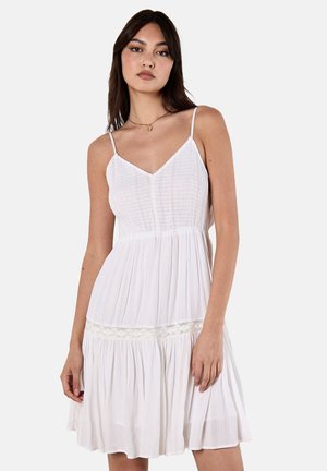 Robe d'été blanche à bretelles spaghetti, dotée d'un corsage texturé, d'une taille froncée et d'une touche de dentelle à l'ourlet. Design fluide.