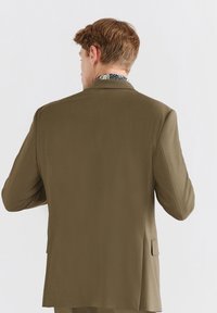 Zielona oliwkowa marynarka o gładkiej fakturze, slim fit i dwóch wentylacji z tyłu. Kołnierz ma kontrastowy, kwiatowy wzór.