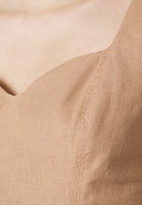 Braunes Leinenoberteil mit V-Ausschnitt und glatter Textur, versehen mit sichtbaren Nähten für einen maßgeschneiderten Look.