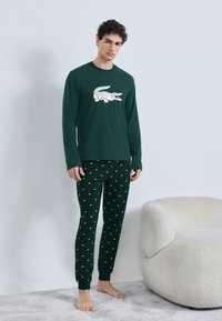 Camiseta de manga larga verde con gráfico blanco de cocodrilo combinada con pantalones de pijama verdes con estampado y pequeños detalles blancos. Tela suave.