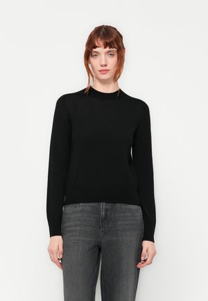Schwarzer Strickpullover mit Rundhalsausschnitt und langen Ärmeln, der eine glatte Textur und eine taillierte Silhouette aufweist, zusammen mit grauen Jeans.
