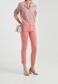 Blusa ligera a rayas rojas y blancas con cuello abotonado, combinada con jeans ajustados rosas y sandalias de tacón bloque nude. Bolso de cuero tipo bandolera.