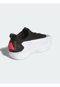 Chaussure de sport noire avec une tige texturée, une semelle intermédiaire blanche et un talon noir à motif accentué de détails rouges.