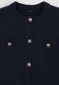 Cardigans lavorati a maglia blu navy con scollo rotondo, bottoni argento e due tasche sul petto con dettagli in bottone. Tessuto testurizzato.