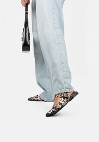 Scarpe flat con stampa leopardata, punta affusolata, fibbie decorate e tacco basso a blocco, abbinate a jeans chiari e una borsa nera.