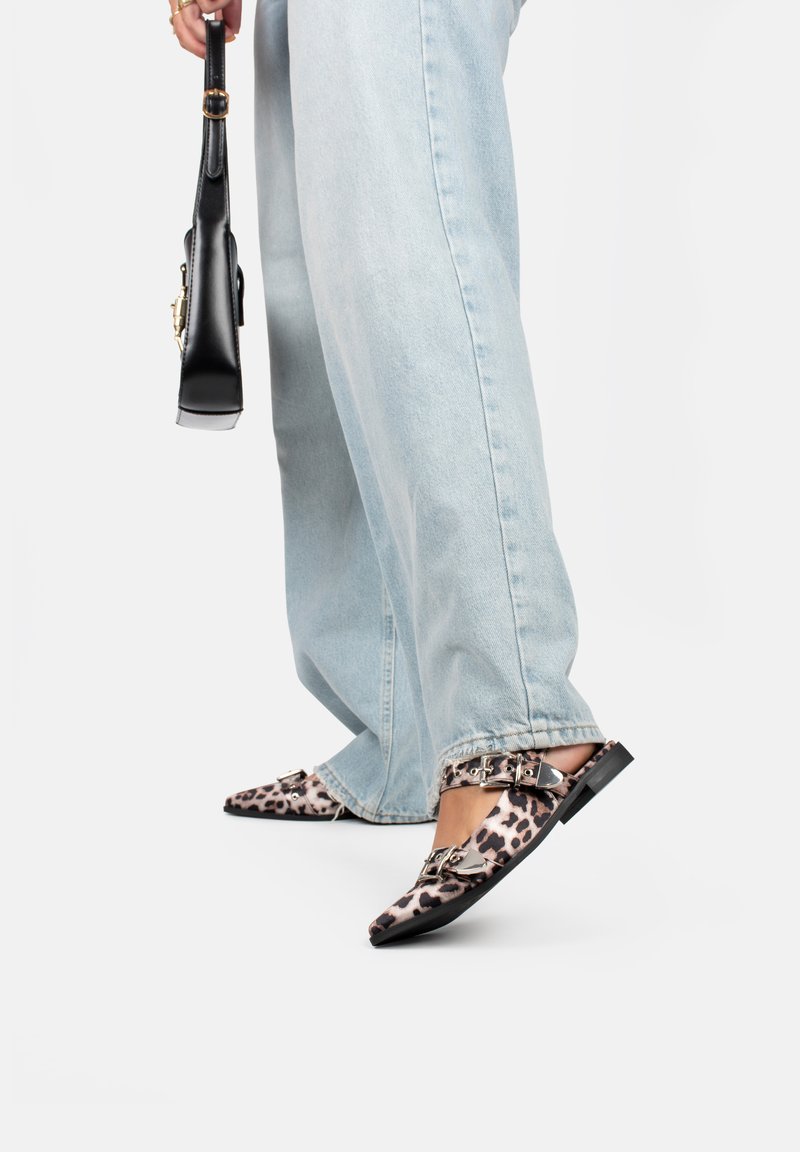 Scarpe flat con stampa leopardata, punta affusolata, fibbie decorate e tacco basso a blocco, abbinate a jeans chiari e una borsa nera.