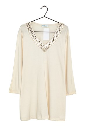 Blouse crème à manches longues avec encolure en V festonnée ornée de sequins noirs et dorés sur un cintre noir.