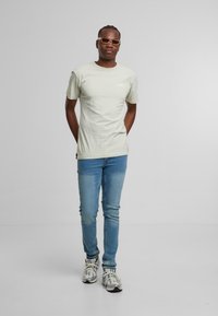 Hellgrünes Baumwoll-T-Shirt, taillierte Passform, kombiniert mit blauen Skinny Jeans. Trägt graue und weiße gemusterte Sneaker und stylische Sonnenbrillen.