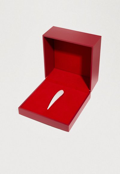 Κόκκινο κουτί με ένα λείο, λευκό αντικείμενο σχήματος δάκρυου μέσα, που ακουμπά σε εσωτερικό από κόκκινο βελούδο. Το κουτί έχει καθαρές, στερεές ακμές.