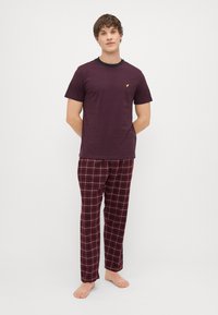 Burgundi T-särk musta kaelusega ja väikese kollase logoga, mille alla on sobitatud tumepunased, sinised ja valged ruudulised öösärgid. Loodud mugavaks kandmiseks, pehme materjal.