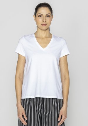 Biała koszulka V-neck z miękkiego materiału, krótki rękaw, w luźnym kroju, zestawiona z czarno-białymi spodniami w paski. Brak widocznych logo.