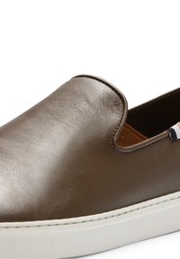 Baskets marron en cuir à enfiler, avec semelle en caoutchouc blanche et petite étiquette en tissu au talon.