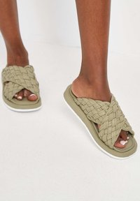 Olijfgroene geweven schuifsandalen met een kruislingse bandontwerp, uitgerust met een rubberen zool met een witte accent. Gladde textuur, casual stijl.