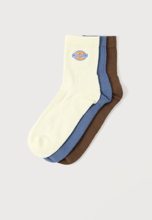 Trīs pāri ribotas zeķes krēmkrāsā, zilā un brūnā, krēmkrāsainajām zeķēm ar apaļu logotipa plāksteri aprocē.