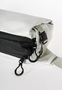Borsa rettangolare grigia con un esterno testurizzato, cerniera nera e tracolla regolabile. Presenta elementi in metallo neri e anelli per attacchi.