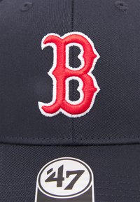 Casquette de baseball marine arborant un imposant logo "B" brodé en rouge, souligné de blanc, avec une étiquette noire circulaire affichant "47".