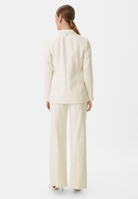 Cream textured blazer with a tailored fit, paired with matching wide-leg trousers, both in a light color palette and minimalistic design.