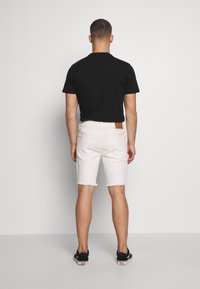 Černé tričko s krátkým rukávem a bílé džíny kraťasy s otrhanými lemy. Výrazná hnědá značka na pásu. Černé boty s bílými podrážkami.