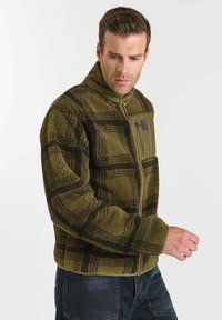 Olijfgroene fleecejas met een geruit patroon, voorzien van een ritssluiting aan de voorkant en een hoge kraag. Zachte textuur, warme ontwerp en zijzakken.