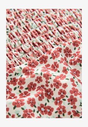 Virágmintás szövet, amelyen apró piros virágok vannak krémszínű háttéren zöld levelekkel; a smockozott textúra redőzött szakaszokat hoz létre.