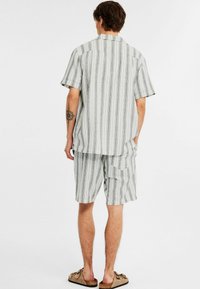 Gestreiftes, hellgraues Kurzarmhemd und passende Shorts aus weichem Stoff. Das Hemd hat einen Camp-Kragen und eine lockere Passform sowie seitliche Taschen.