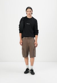 Black sweatshirt with white embroidery, brown cargo shorts with front pockets, black shoes, and white socks. Plain background.