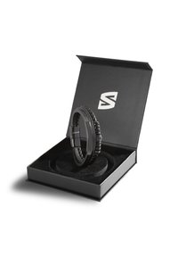 Schwarzes Lederarmband, präsentiert in einer schwarzen Box mit weichem Innenbereich. Das Armband hat geflochtene und glatte Abschnitte, einen sicheren Verschluss sowie geprägte Details.