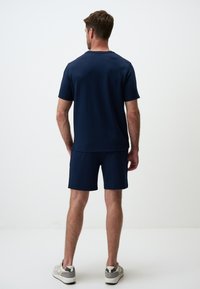 Granatowa koszulka z krótkim rękawem i dopasowane szorty, wykonane z gładkiego materiału, cechujące się luźnym krojem i prostym fasonem.